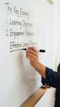 Female teacher writing effective lesson planning on whiteboard in classroom