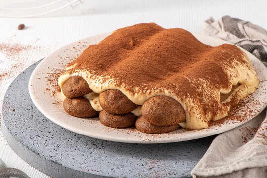 Homemade tiramisu cake on a ceramic plate with cocoa powder