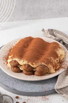 Homemade tiramisu cake on a ceramic plate with cocoa powder vertical view