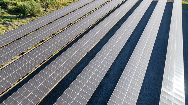 Large solar farm with rows of photovoltaic panels set against a backdrop of lush green forest and distant mountains in Itaguai, Rio de Janeiro, Brazil. Aerial view.