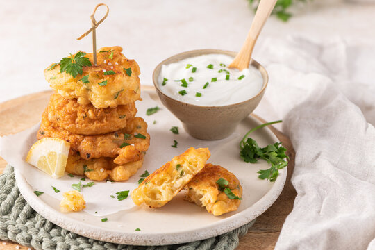 Crispy golden cod fish fritters stacked on a rustic plate with a creamy dipping sauce and fresh herbs for an elegant Mediterranean style appetizer