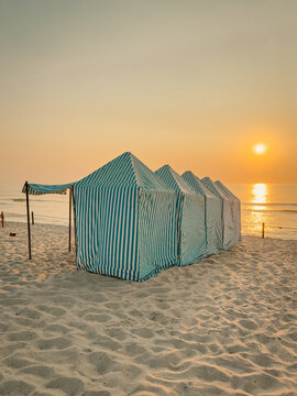 Striped beach tents on sandy coast at warm sunset
