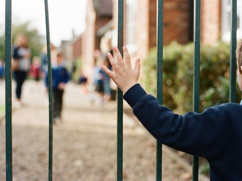 Young boy standing behind school metal fence reaching out hand concept of separation and education