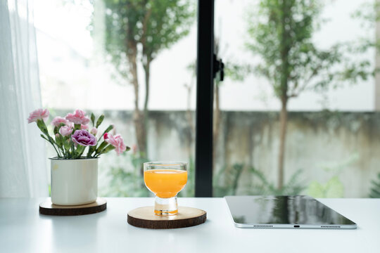 Orange juice and tablet and pink flowers arranged on white desk