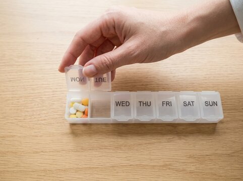 Woman organizing daily medication pills in a weekly plastic organizer box on a wooden table