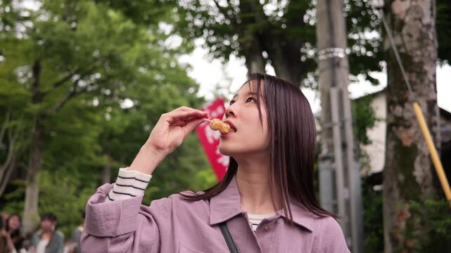 東京のレトロな観光地（深大寺近くの公道）でお団子を食べる笑顔の女性
