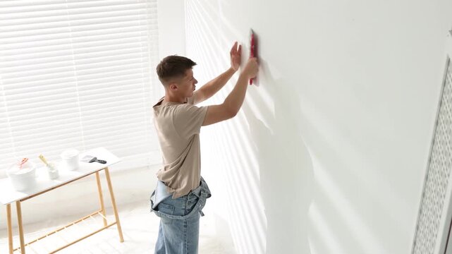 Handyman plastering white wall with putty knife indoors
