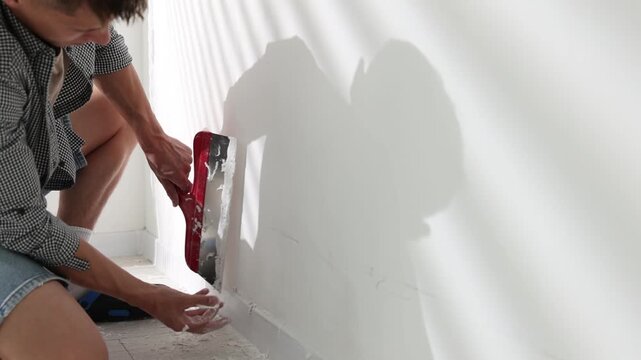 Handyman plastering white wall with putty knife indoors, closeup