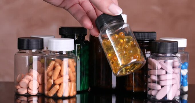 Woman showing medical bottles with pills and putting them onto mirror table against beige background, closeup