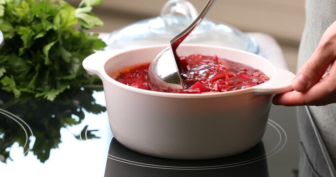 Woman mixing tasty borscht in pot with ladle at stove, closeup