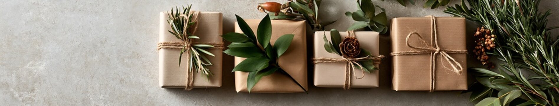 Eco friendly kraft paper gift boxes tied with twine and botanical sprigs on textured concrete background