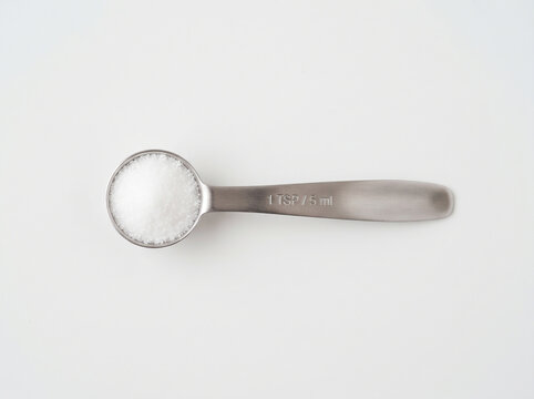 Teaspoon filled with white salt isolated on white