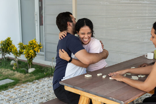 Young couple hugging and laughing outdoors playing dominoes