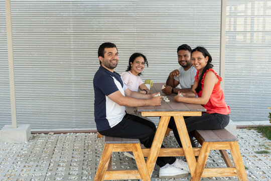 Young adults playing dominoes at outdoor table, smiling