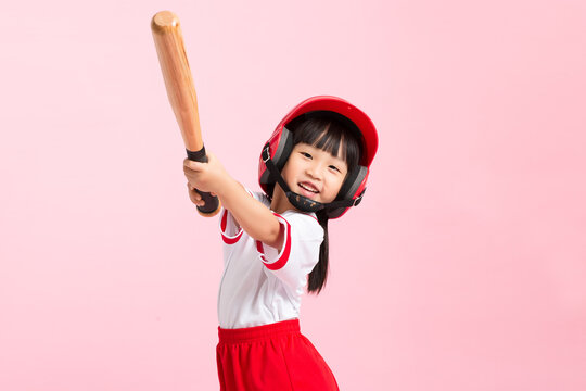 Close up of a smiling young girl in a red helmet practicing her baseball swing in studio.