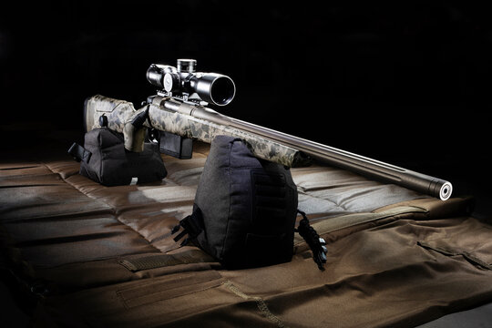 Rifle with a large riflescope on a beige and brown shooting mat