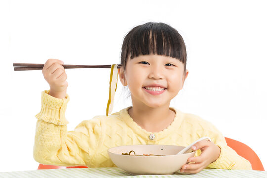 Happy Asian Little Girl Eating Noodles with Chopsticks at Dining Table Isolated on White Background