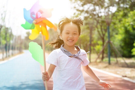 Cheerful little girl running forward while holding a colorful pinwheel toy on a park path.