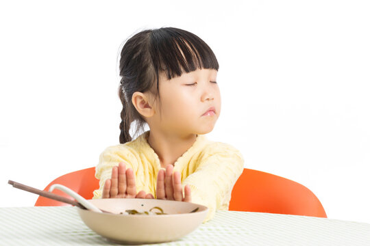Asian Little Girl Refusing to Eat at Dining Table with Unhappy Expression Isolated on White Background
