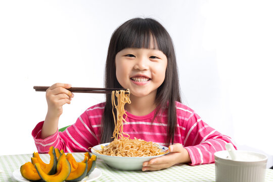 Happy Asian Little Girl Eating Noodles with Chopsticks at Dining Table Isolated on White Background