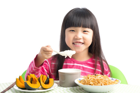 Happy Asian Little Girl Eating Porridge with Spoon at Dining Table Isolated on White Background