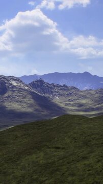 Rolling hills lead to towering mountains bathed in sunlight, their rugged peaks reaching for the sky. Lush green valleys provide a vibrant contrast to the rocky terrain, creating a serene scene.