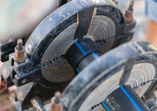 Close-up of black HDPE pipes joined together using a hydraulic butt fusion welding clamp machine on a work site.