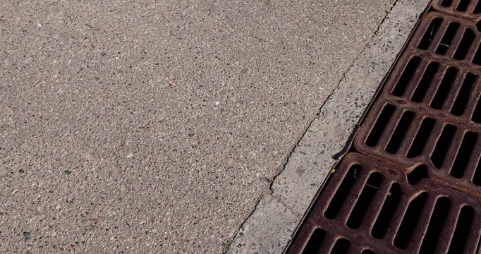  metal storm drain grate on asphalt, old drainage grate is installed along the edge of a city road, storm drain