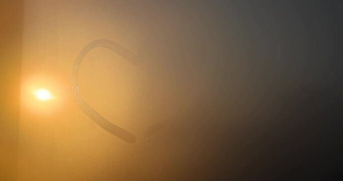 The warm disk of the sun behind the wet window glass, the yellow sun is visible through small transparent drops of water in the evening , glass with a heart pattern