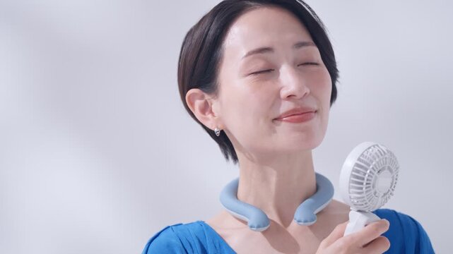 夏にアイスリングとハンディ扇風機を使う女性