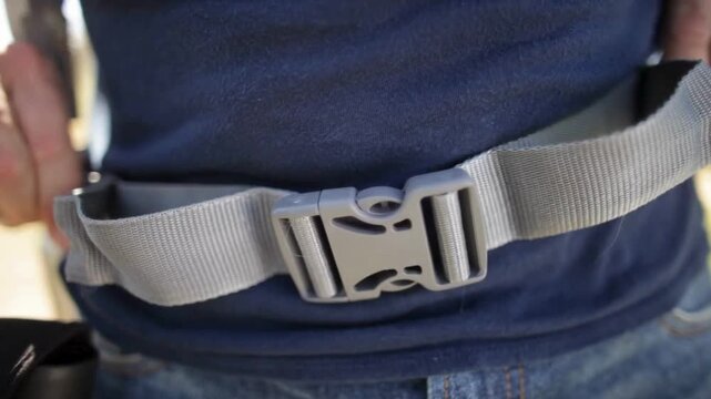Close up of hands fastening a grey plastic quick release buckle on a utility waist belt.