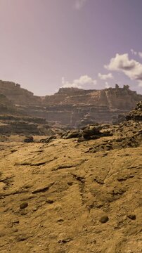 Golden sunlight casts a warm glow over sprawling rocky terrain. Majestic cliffs tower above, creating a stunning contrast against the clear blue sky.