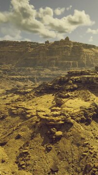 Golden hues blanket the desert landscape, revealing striking stone formations. The vast terrain stretches endlessly, with hills rising dramatically against a backdrop of fluffy clouds.