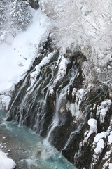 Frozen waterfall cascading over rocks in a snowy gorge © SUPAPONG
