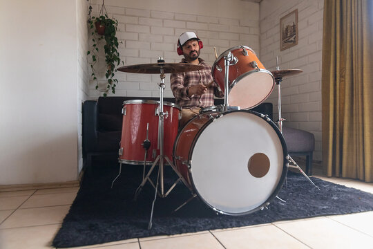 A man wearing headphones practices songs on his acoustic drum set, a percussion instrument