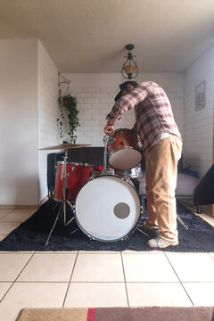 A man is setting up an acoustic drum set at home