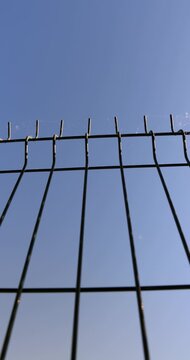 Dark metal mesh fence against clear blue sky, welded wire fencing structure installed outdoors under bright sunlight on sunny summer day