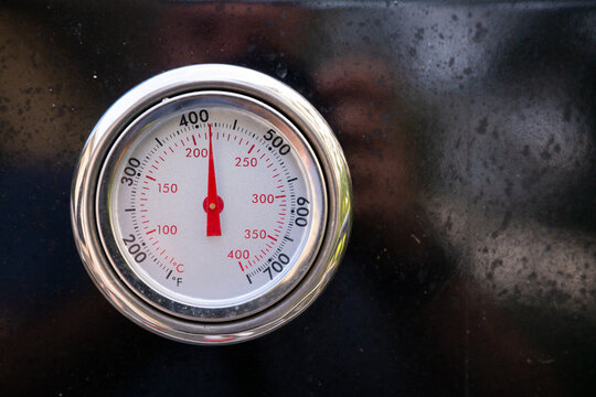 Close-up of a temperature gauge on a black outdoor barbecue grill during summer cooking.