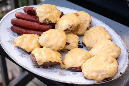 Fresh grilled cheeseburgers and hot dogs arranged on a serving plate during an outdoor cookout or barbecue.
