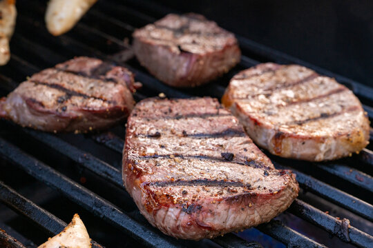Close up of steaks cooking on a barbecue grill with visible grill marks and shallow depth of field.