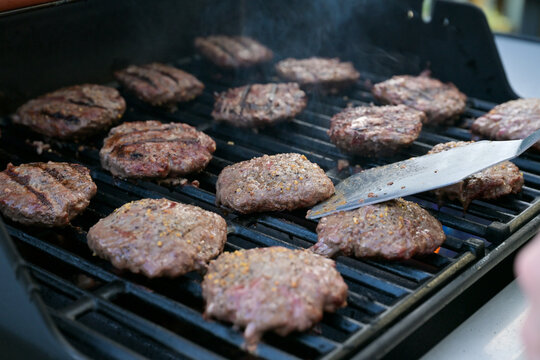 Hamburger patties and hot dogs cooking on a smoky outdoor barbecue grill during a backyard cookout.