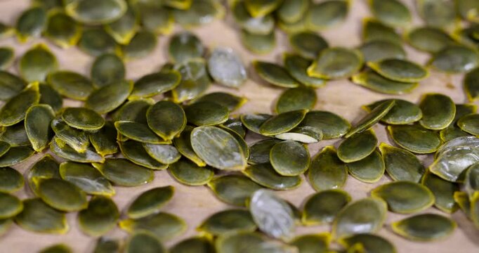 Dark green pumpkin seeds on a brown paper surface, wet fresh pumpkin seeds drying on parchment paper on the kitchen table