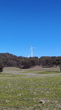 Wind Turbines Spinning on Green Hills Under Clear Blue Sky