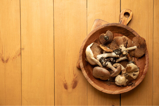 Mushrooms of various types are displayed in a round wooden bowl on a natural wood surface