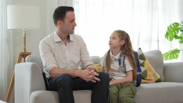Father and daughter talking sitting on sofa at home with school backpack, Dad having conversation with little school girl on couch in living room, Parent talking to child before school