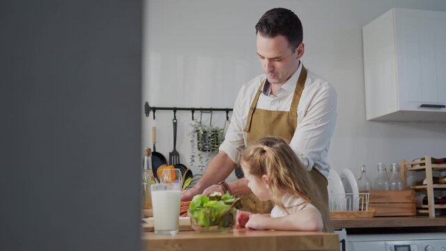 Happy young girl helping father cook meal at home, Father and daughter preparing healthy food together in modern kitchen, Family time cooking concept with dad and daughter in domestic kitchen