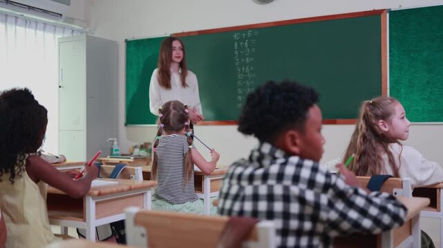 Teacher and elementary pupils during math lesson in school, Diverse students in classroom, Engaged children in classroom activity with teacher at blackboard