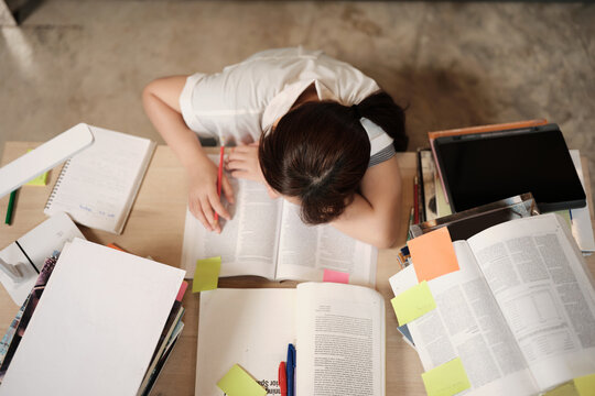 College Asian teenage girl tired and burned out from overwhelmed study pile of books, stressed learning at home with stack of textbooks, reading and writing for school exam, homeschooling education.