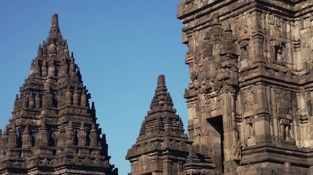 Multiple Prambanan Temple spires emerge between ornate stone structures, creating a dramatic historic skyline.