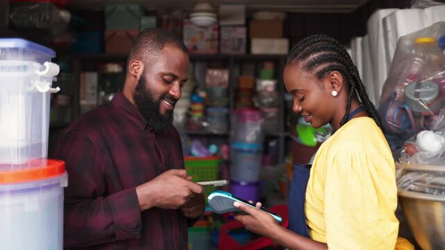 African small business owner facilitating a contactless transaction with a smartphone and POS device in her shop